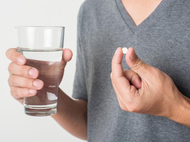 Mann hält Glas mit Wasser und Tablette gegen Herz-Kreislauferkrankungen in Händen