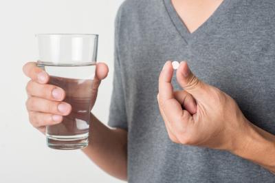 Mann hält Glas mit Wasser und Tablette gegen Herz-Kreislauferkrankungen in Händen